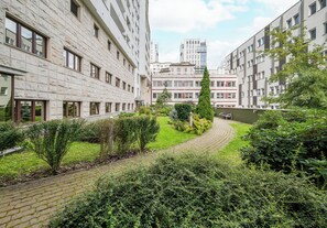 Une cour avec un chemin pavé, entourée d’immeubles à plusieurs étages dotés de grandes fenêtres et d’un arbre au centre.