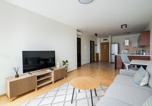 Ein modernes Wohnzimmer mit Flachbildfernseher, Holz-Unterhaltungseinheit und grauem Sofa mit gemustertem Überwurf.