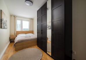 Een slaapkamer met een bed, nachtkastje, raam met gordijnen, kledingkast en een rond tapijt.