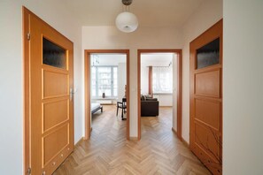 Ein Flur mit Holztüren, einem Fischgrätparkett und Blick in einen Wohnbereich mit Sofa und Tisch.