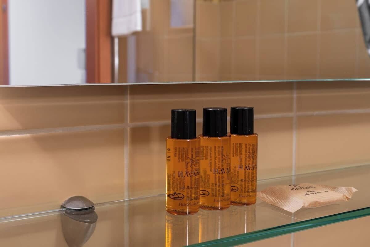 Three bottles of hair oil on a glass shelf in a bathroom with beige tiles.