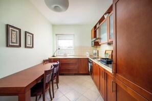 A compact kitchen with wooden cabinets, a dining table, and chairs. - Wyględowska 2-Bedroom Apartment (Warszawa)