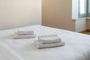 A neatly made bed with folded white towels and a window with blinds. - Wyględowska 2-Bedroom Apartment (Warszawa)