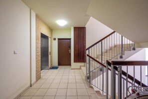 Ein Flur mit gefliestem Boden, einer Holztür, einem Metallgeländer und einer Treppe.