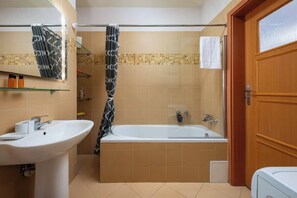 Een badkamer met een wit wastafelmeubel, een bad en een douchegordijn.