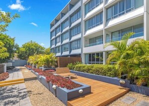 Un hôtel moderne à l’architecture contemporaine, doté d’une structure à plusieurs étages, d’une terrasse en bois extérieure et d’espaces paysagers aménagés en jardin.