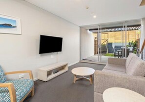 Un salon moderne doté d’un téléviseur à écran plat, d’un canapé, d’une table basse et d’une porte-fenêtre coulissante donnant sur un espace extérieur.