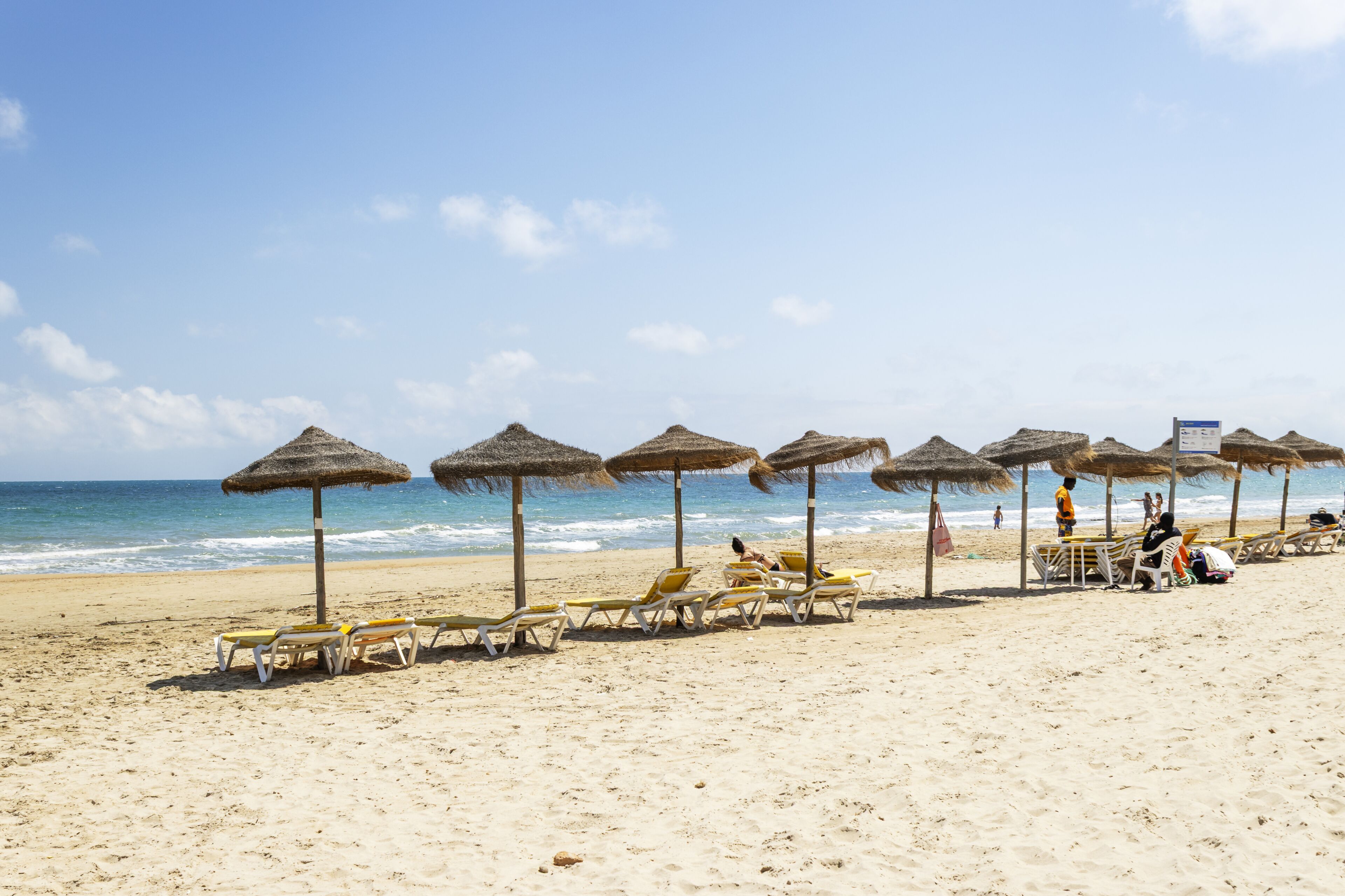 A beach with sun loungers and thatched umbrellas.
