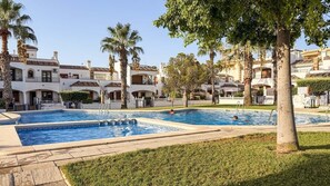 Un área de piscina con varias piscinas, palmeras y un edificio con balcones.