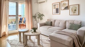 A living room with a sofa, two side tables, a potted plant, and artwork on the wall. - Pink La Perla Apartment (Zenia, La)