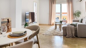 Una sala de estar con un sofá, una mesa de comedor con sillas, un televisor y una ventana con cortinas.