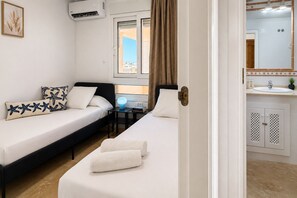A hotel room with two beds, a desk, a window with curtains, a bathroom with a sink and cabinets, and a framed picture on the wall. - Pink La Perla Apartment (Zenia, La)