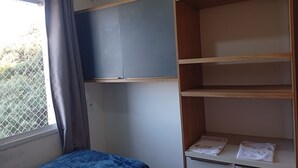 Habitació amb un llit, una finestra amb cortines i una estant de fusta amb una tovallola.
