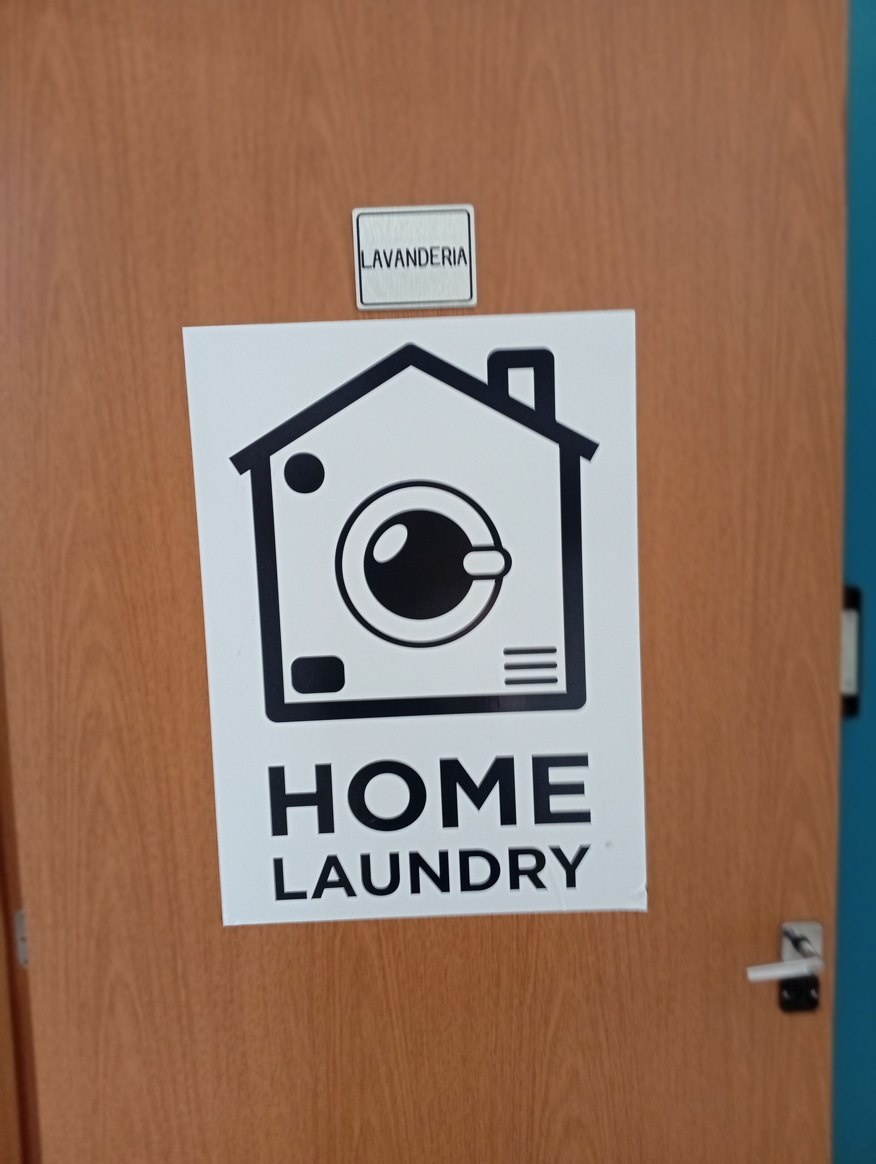 A door with a white sign that reads 'HOME LAUNDRY' and a smaller sign above it that says 'LAVANDERIA.'