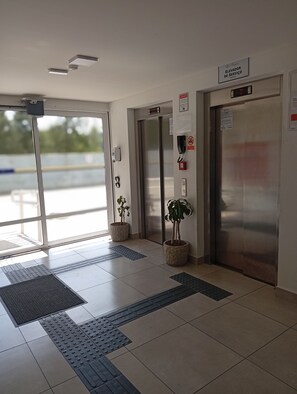 An elevator area with two elevators, a fire alarm, a telephone, and tactile paving on the floor.