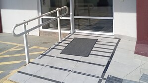Entrada d'un edifici amb rampa, porta i superfície tàctil al terra.