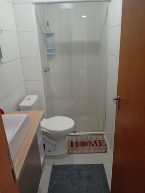 A small bathroom with a toilet, a shower enclosure, and a wooden door. - Cozy apartment with complete security in the Serra Gaúcha region, within the UniverUCS campus. (Caxias do Sul)