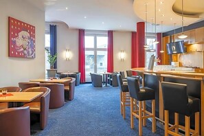 Een restaurantgedeelte in een hotel, met tafels, stoelen, een bar en een schilderij aan de muur.