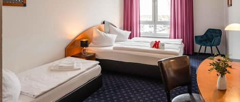 A hotel room with two single beds, a small table with a vase, and a chair.