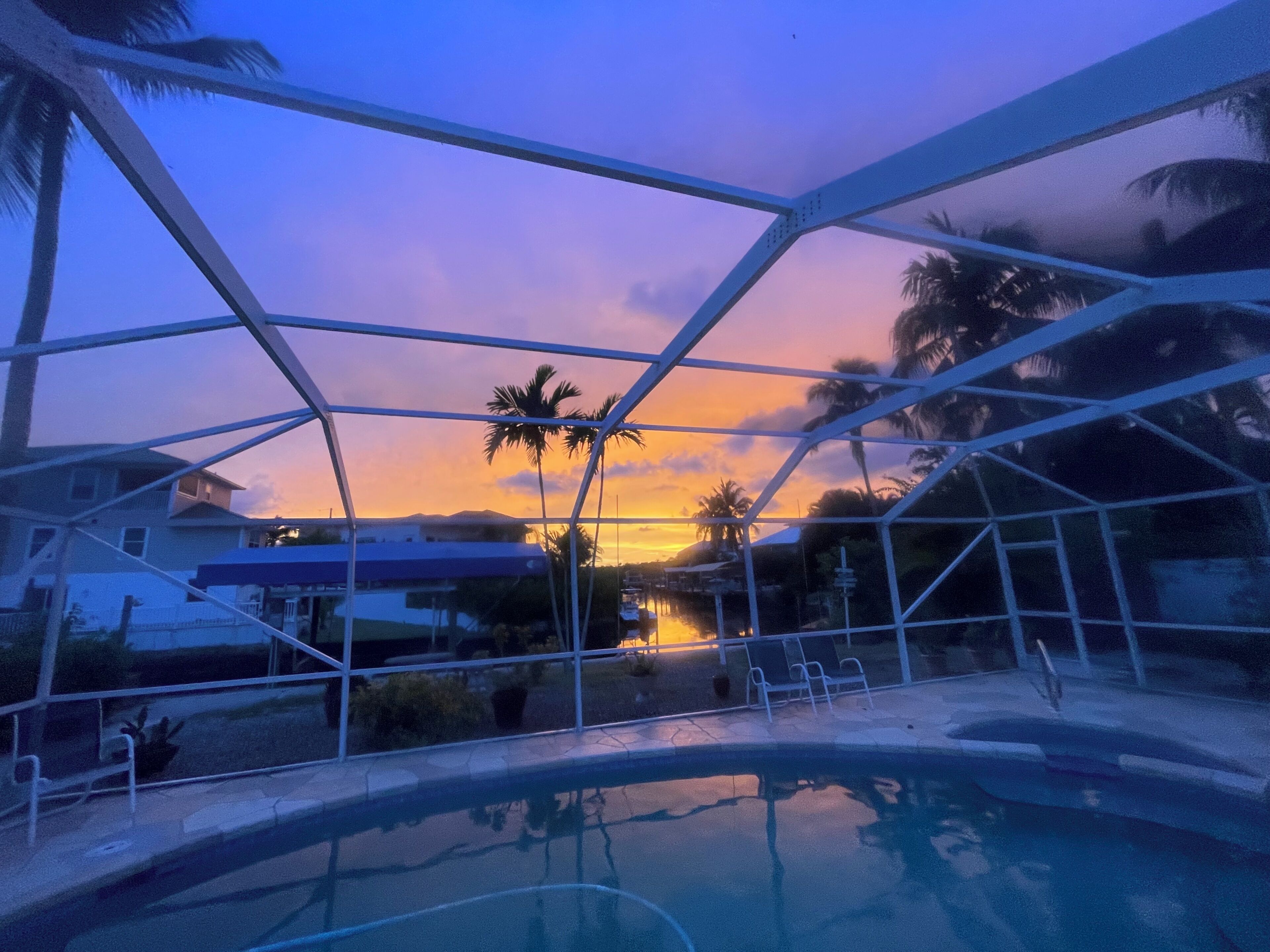 Zona de piscina con vistas a palmeras y un atardecer.