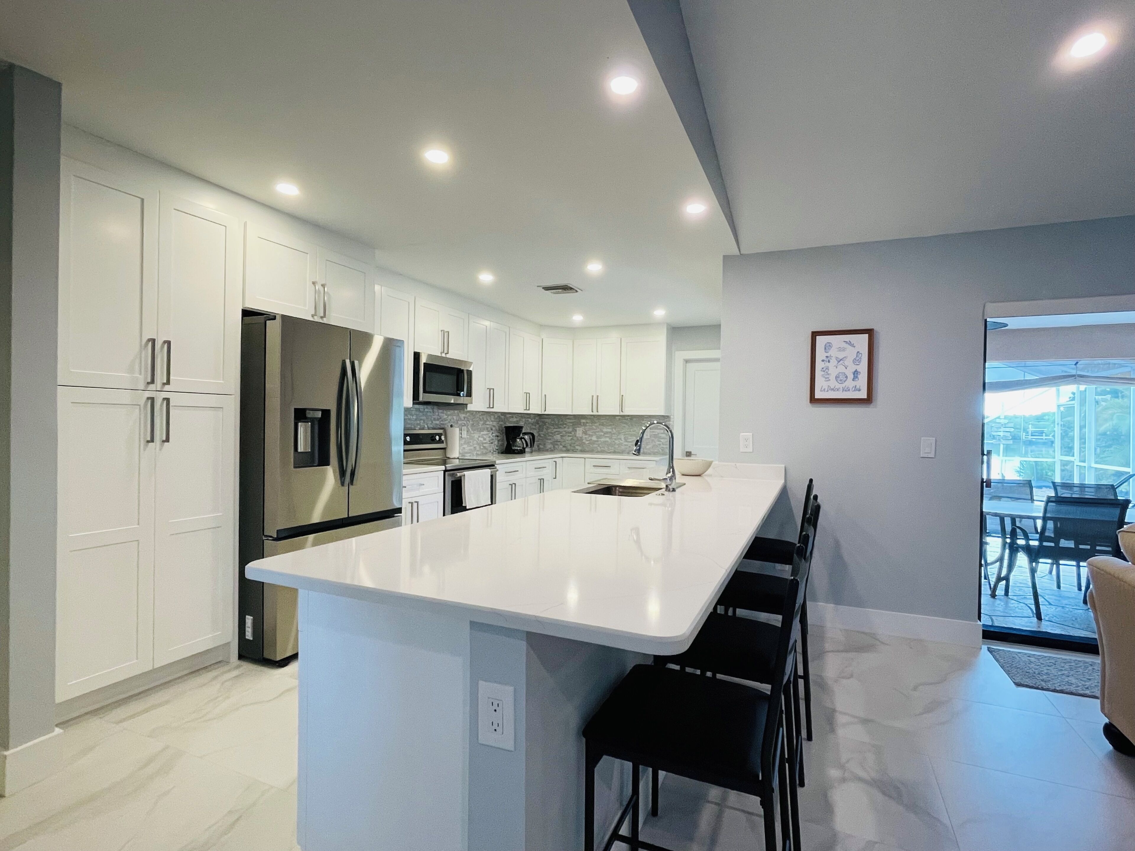 Une cuisine moderne avec des meubles blancs, des appareils en acier inoxydable et un grand îlot central doté de tabourets de bar.
