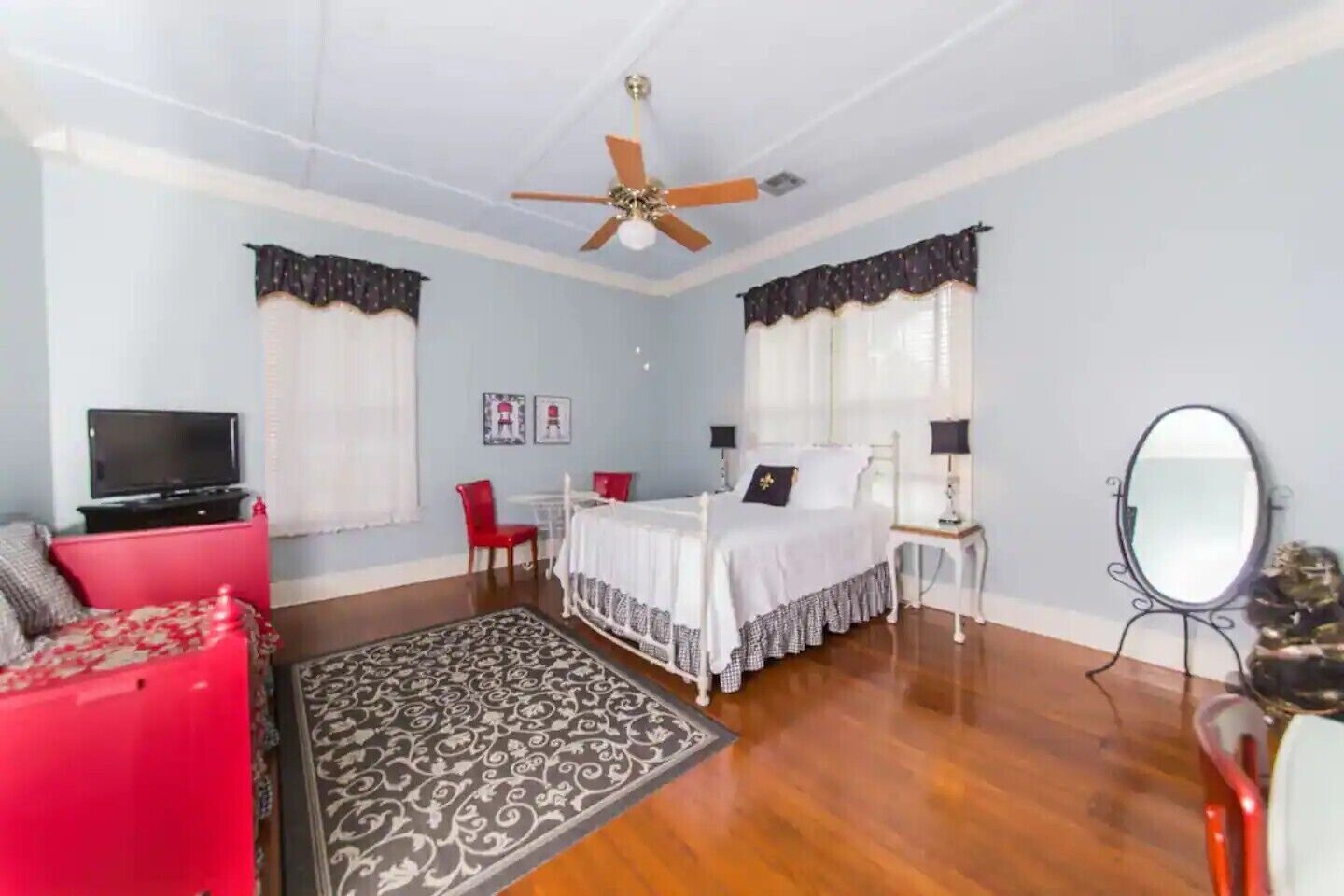 A bedroom with a bed, a television, a red chair, a desk, and a ceiling fan.