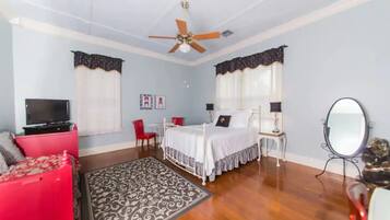 A bedroom with a bed, a television, a red chair, a desk, and a ceiling fan.