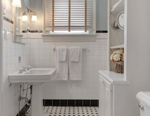 Une salle de bain avec un lavabo blanc, un miroir et une fenêtre avec des stores.