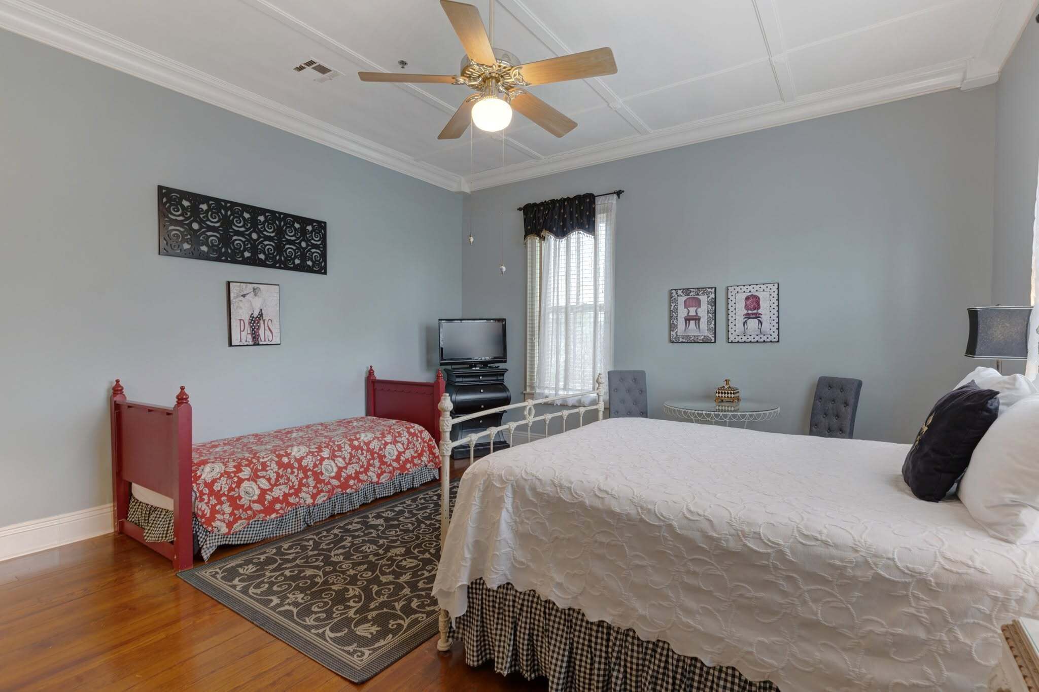 Une chambre avec deux lits, un ventilateur de plafond, une télévision et des œuvres d’art décoratives au mur.