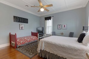 A bedroom with two beds, a ceiling fan, a television, and decorative wall art.
