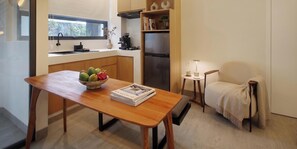 Une cuisine de taille modeste avec une table en bois, un saladier rempli de fruits, une petite table d’appoint avec une lampe et une chaise recouverte d’une couverture.
