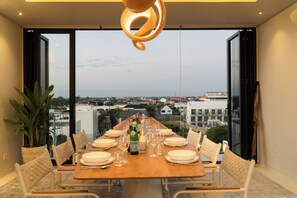 Mesa de comedor dispuesta para seis personas, con sillas, una botella de agua Pellegrino y copas de vino.