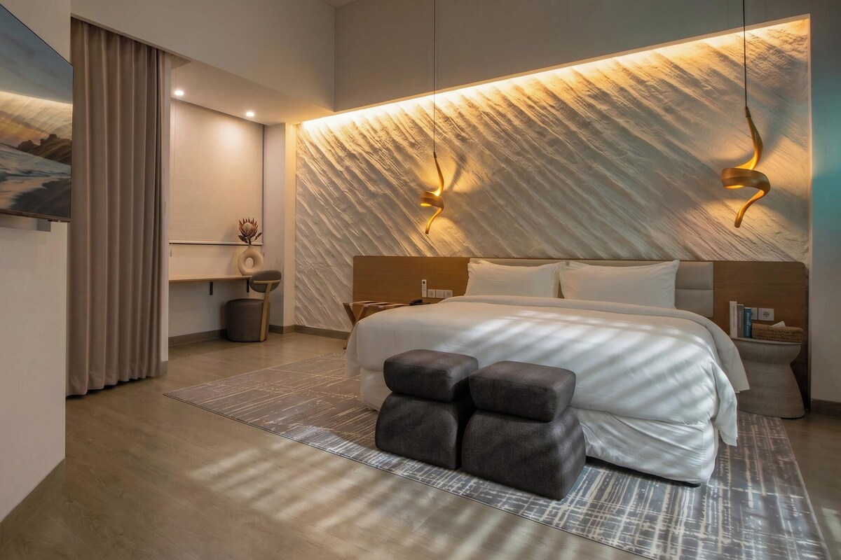 Une chambre moderne avec un grand lit, une tête de lit dotée d’un éclairage intégré, une table de chevet et une œuvre d’art accrochée au mur.