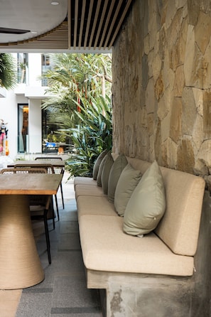 A modern outdoor seating area with a stone wall, a wooden table, and a sofa with cushions. - Echo Beach Suites - Canggu (Badung)