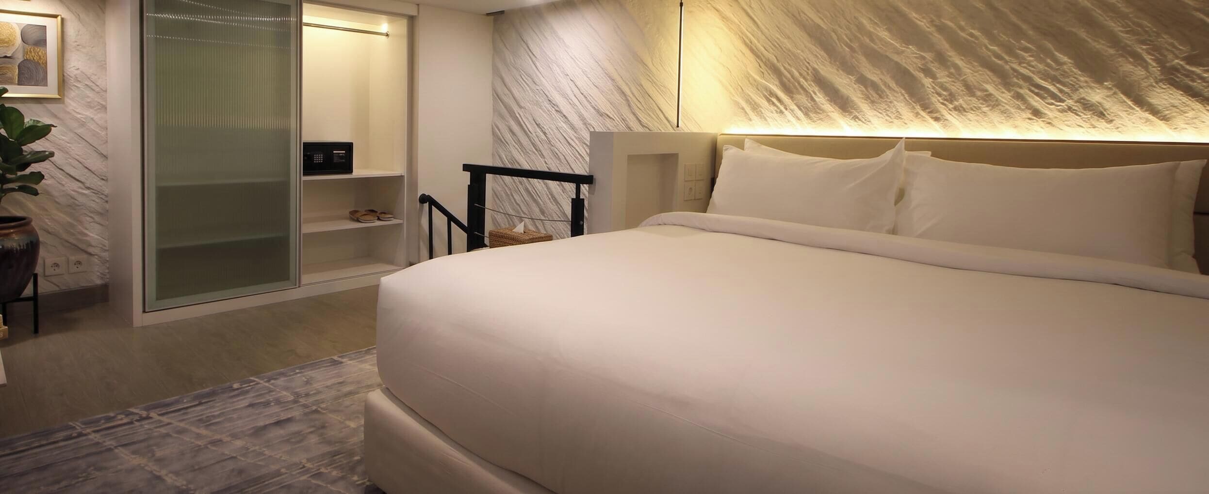 Ein Hotelzimmer mit einem großen Bett, einem begehbaren Kleiderschrank und einer an der Wand befestigten Ablagefläche.