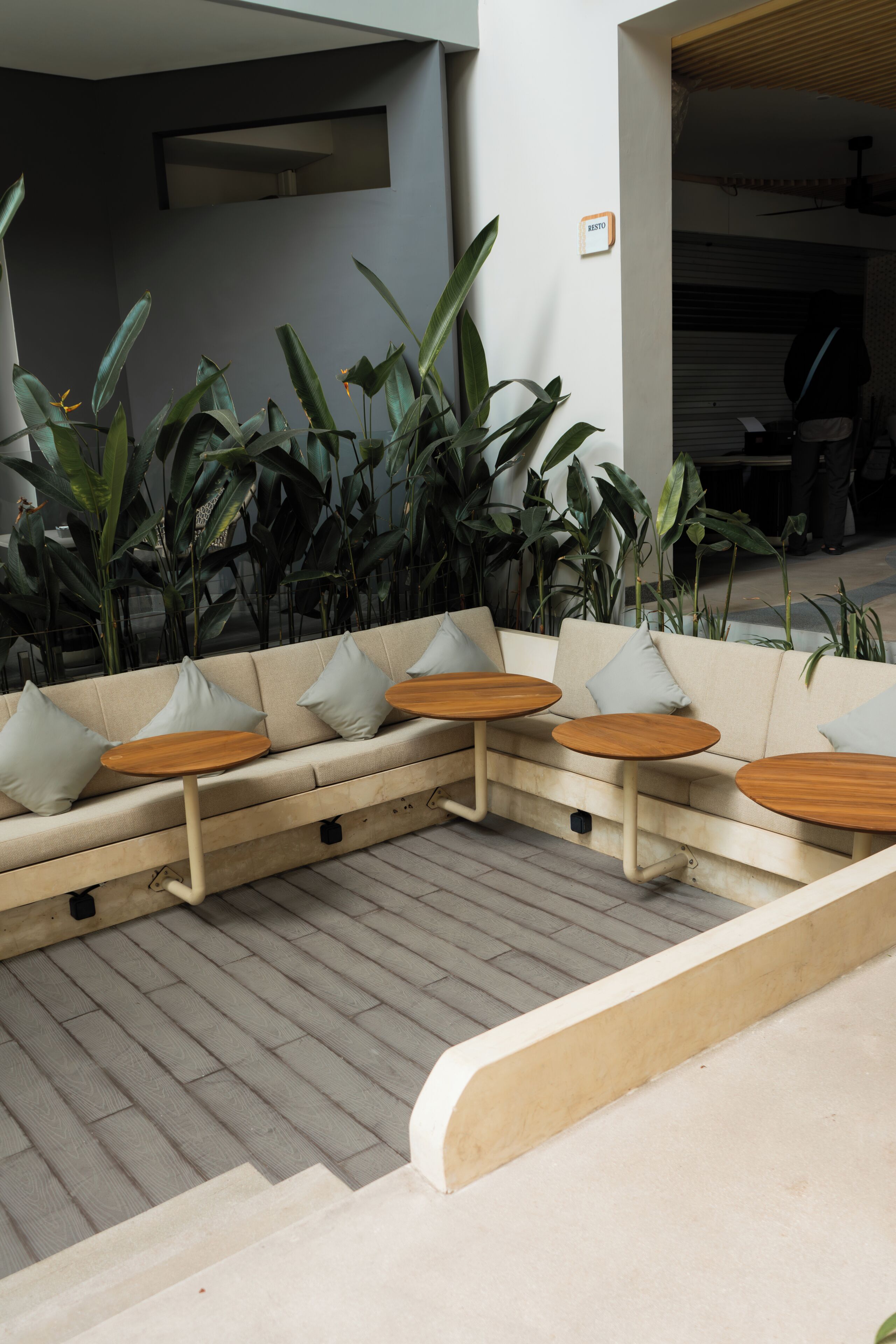 Un espace extérieur moderne aménagé avec des sièges, comprenant un canapé et des tables rondes, le tout entouré de grandes plantes vertes.
