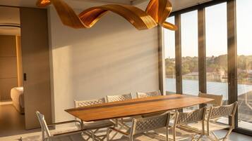 Un comedor moderno con una mesa de madera y sillas blancas, ventanas amplias y vistas al exterior.