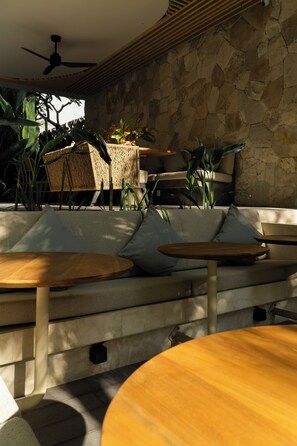 Un área de estar exterior moderna con paredes de piedra, ventilador de techo y diversas plantas.
