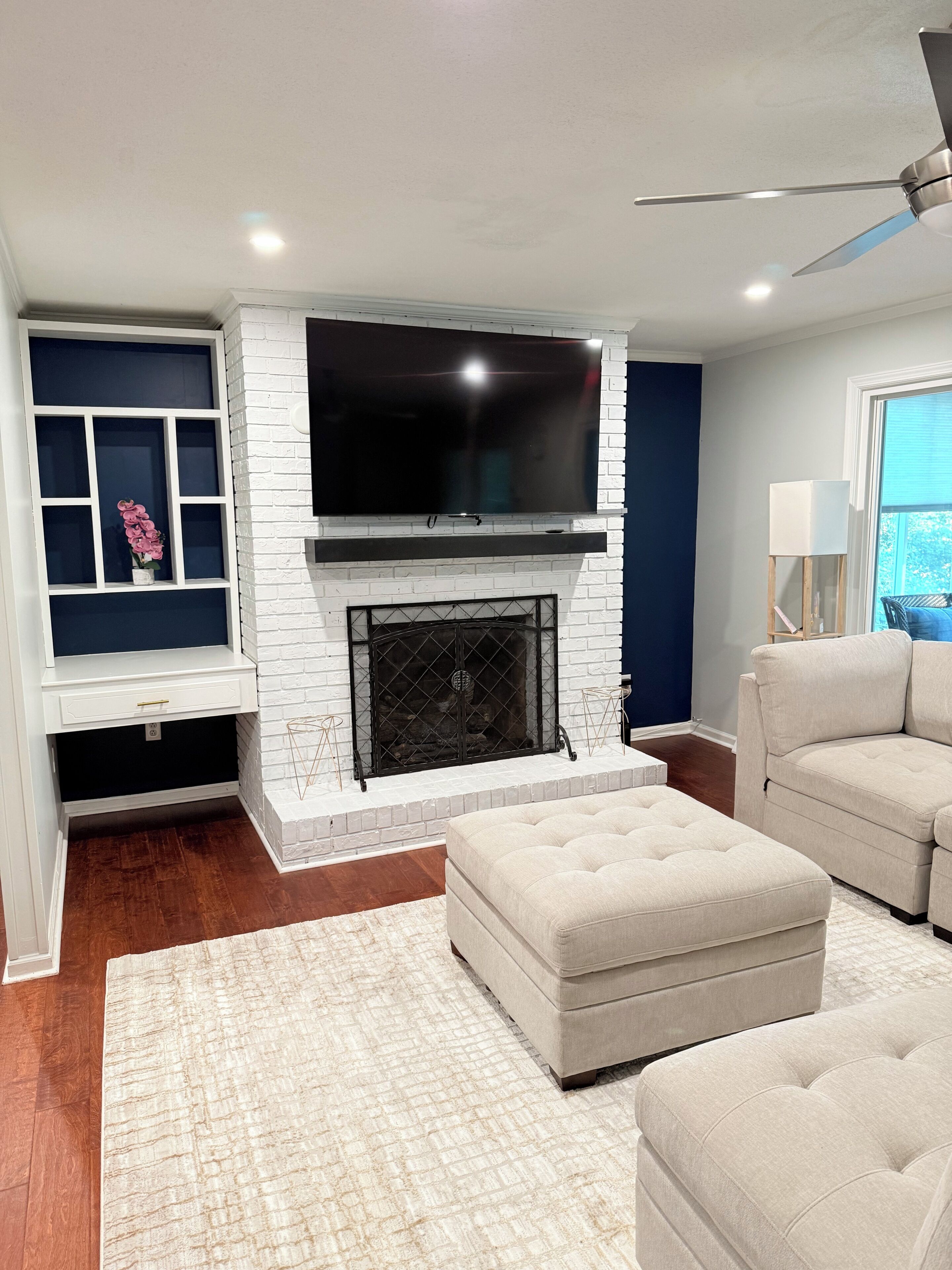 A modern living room with a fireplace, a flat-screen TV mounted above it, and a ceiling fan.