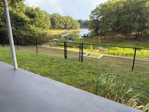 A concrete balcony with a metal railing overlooking a grassy area with trees and a body of water.