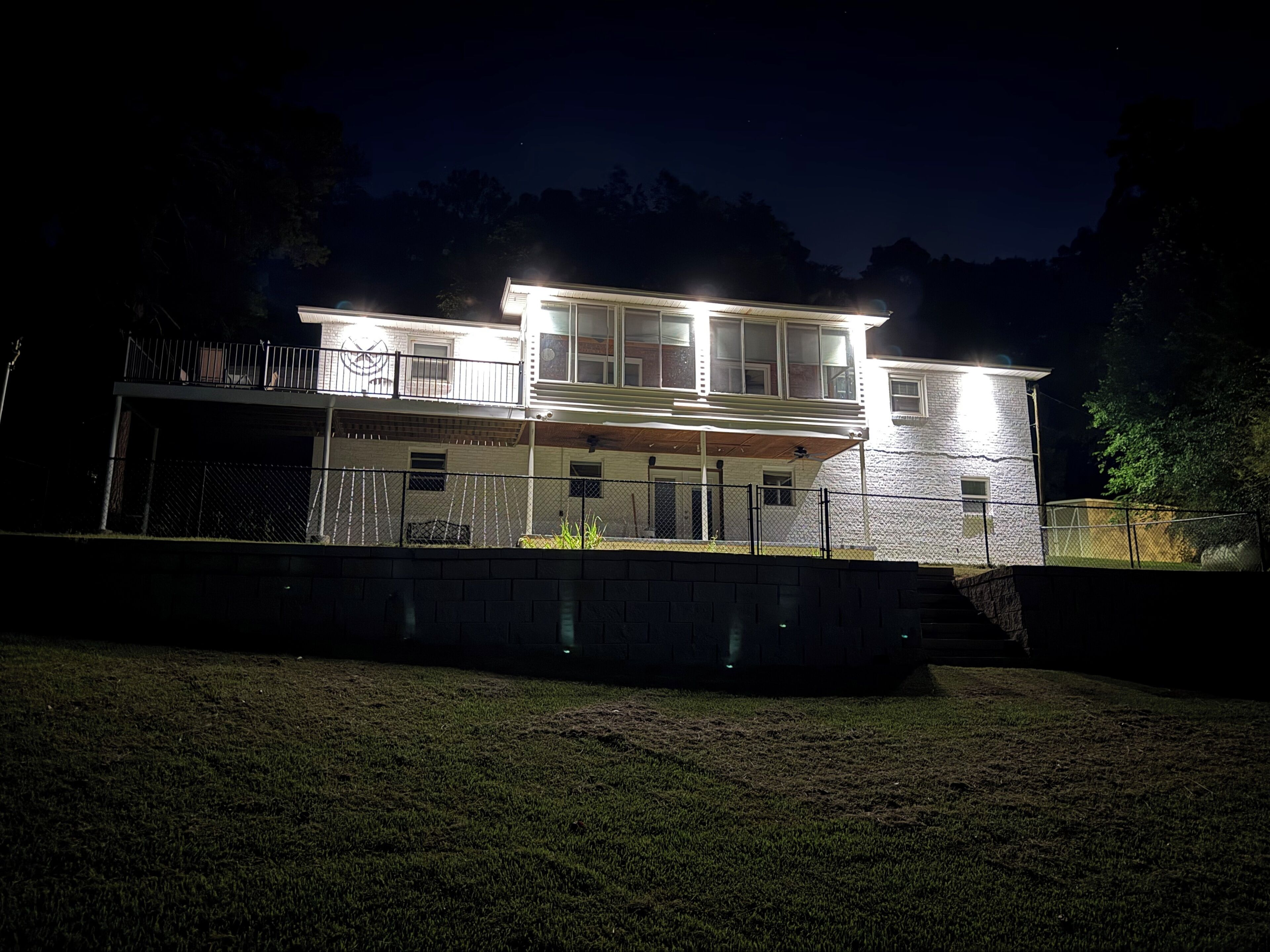 A two-story house with a covered porch and a fenced yard at night.