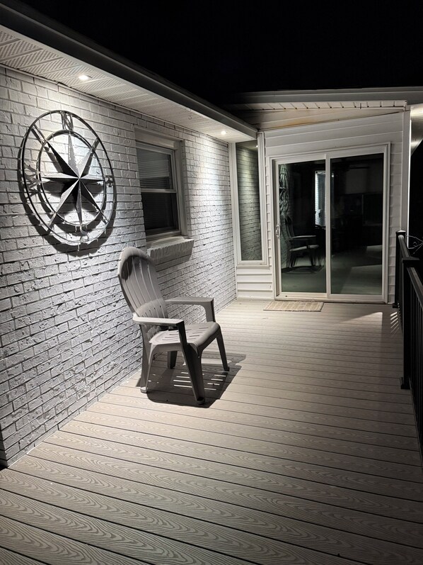 A covered outdoor area with a brick wall, a metal wind direction indicator, a plastic chair, and a sliding glass door leading to an interior space.