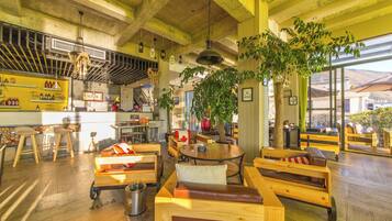 Un café acogedor con mobiliario de madera, una zona de bar y amplios ventanales que dejan entrar luz natural.