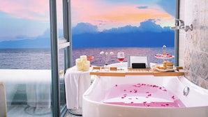 Un baño con una bañera llena de agua, una mesa con velas, una copa de vino tinto y una bandeja con aperitivos.