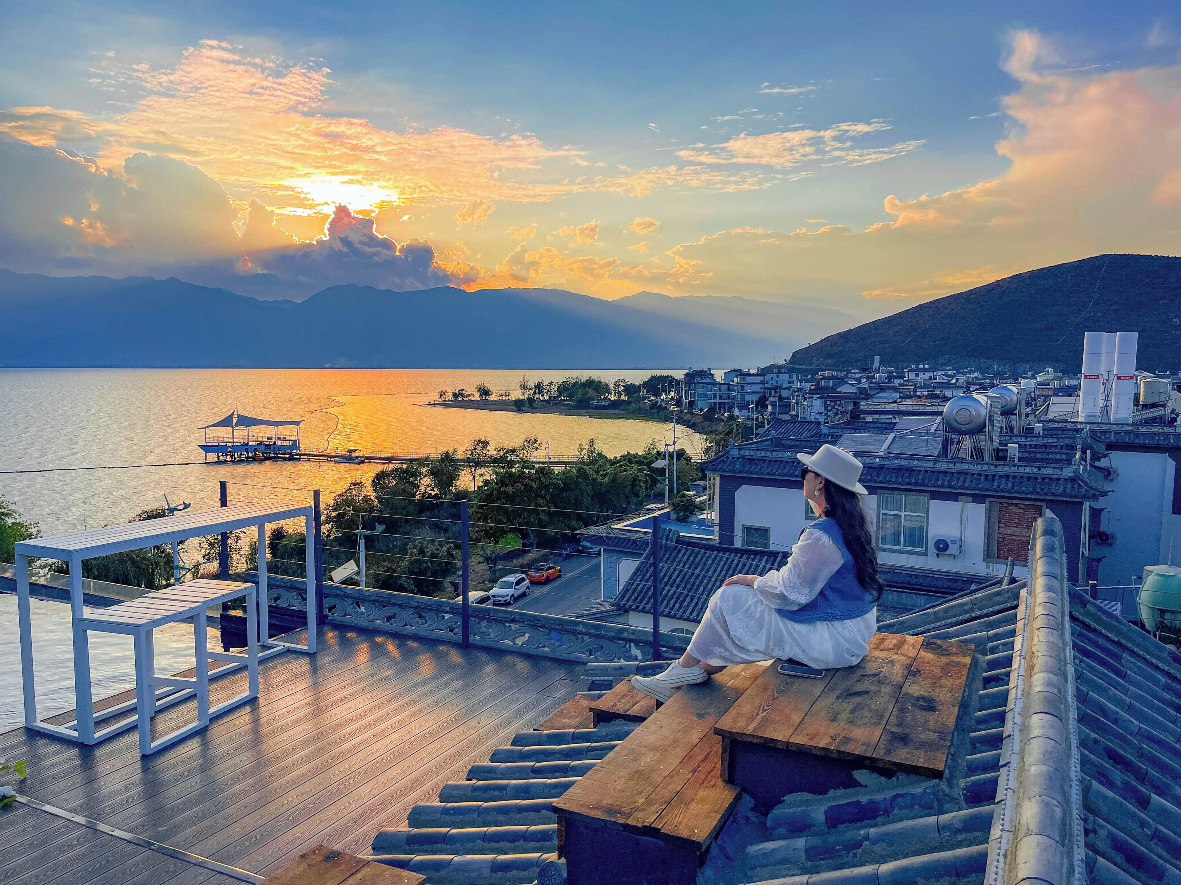 A person sitting on a wooden deck overlooking a body of water with a cityscape in the distance.