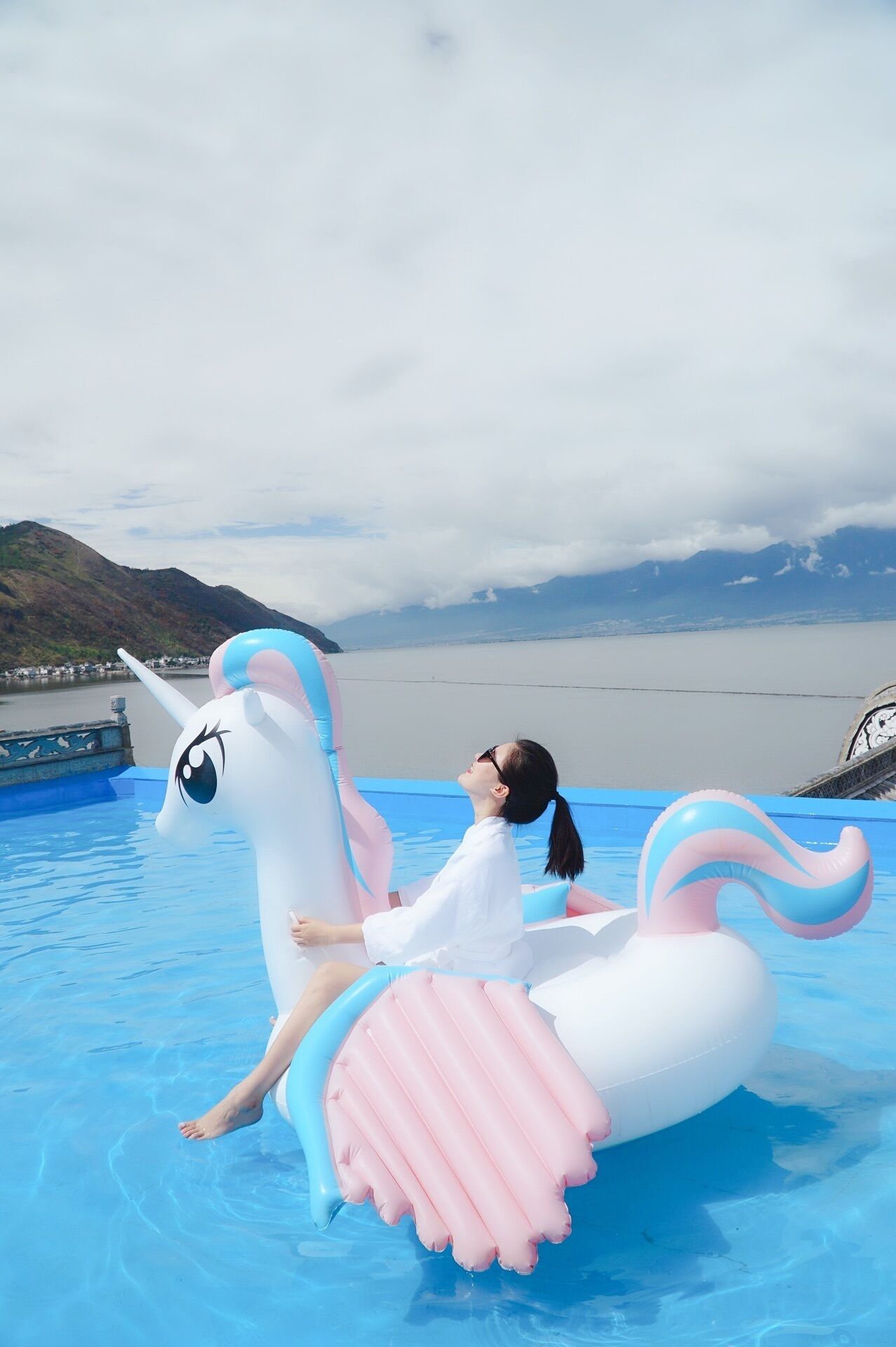 A person on a unicorn float in a pool with a mountainous backdrop.
