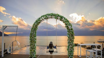 Una terraza de madera con un parque infantil y una mecedora bajo un arco decorado con flores blancas.