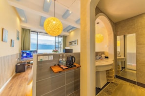 A hotel room with a large window, a flat-screen TV, a coffee maker, and a sink.