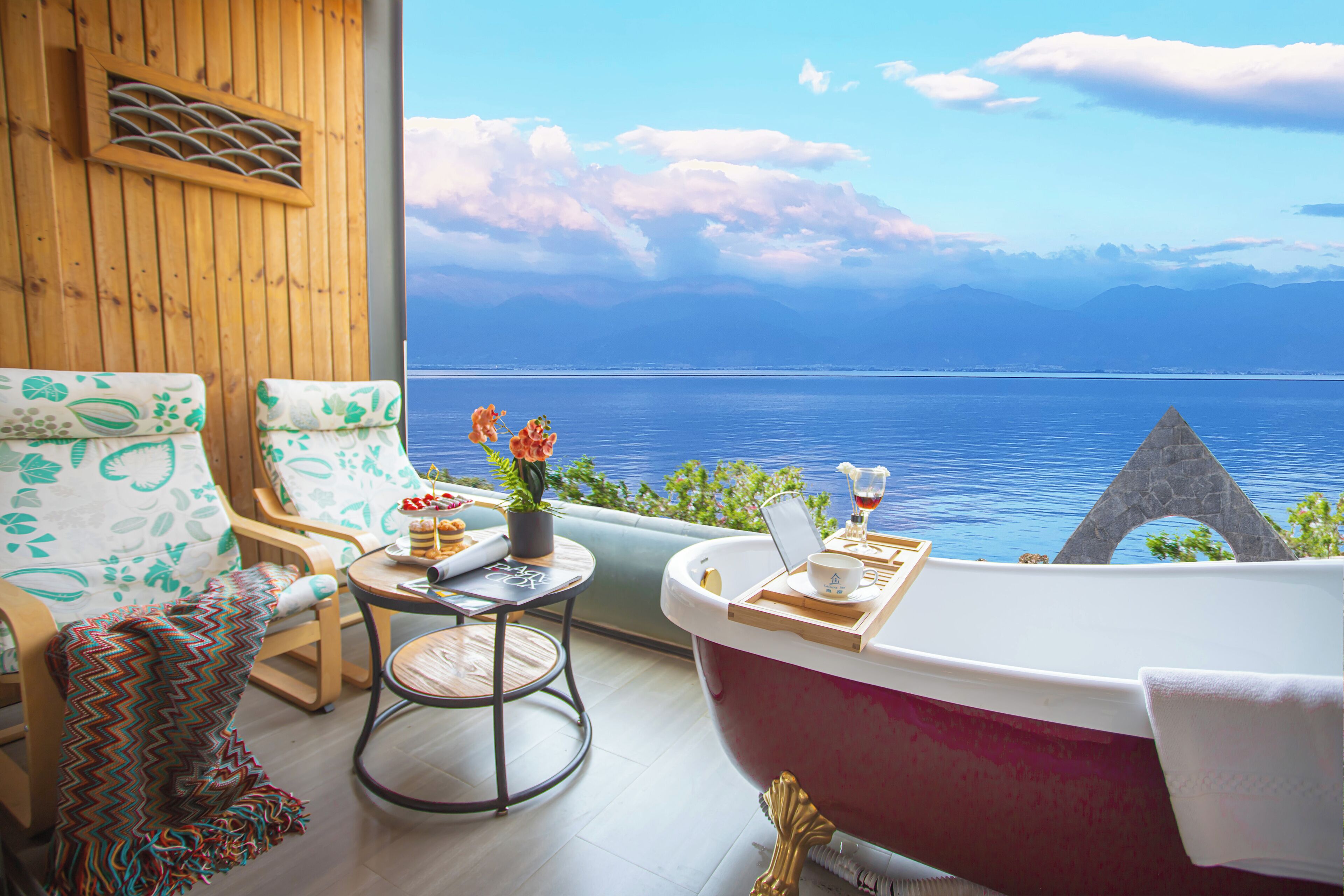Una habitación con una bañera grande, una pared de madera y vistas al mar, además de una mesa con una bandeja.