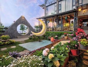A garden with a crescent-shaped light fixture, a stone archway, and various potted plants.